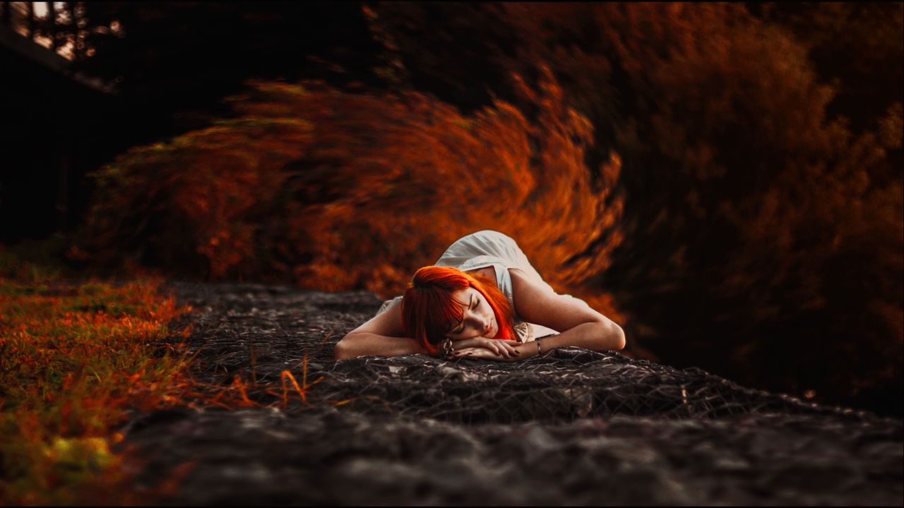 A woman with red hair peacefully resting in a vibrant autumn setting.