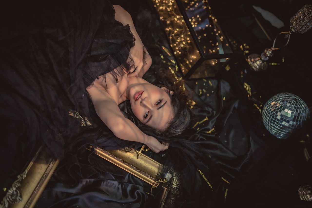 Artistic portrait of a woman lying amid black fabric with golden accents and lights.